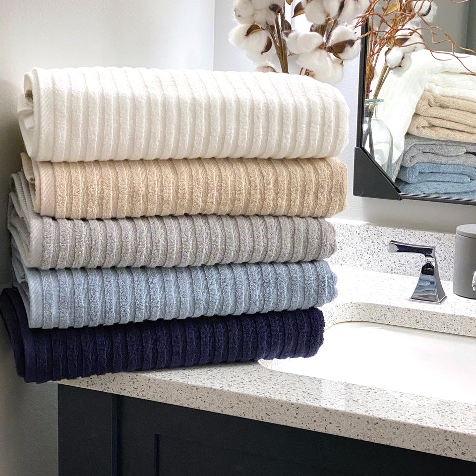 Multiple colors of the American Choice Ribbed towels stacked neatly on a bathroom counter.