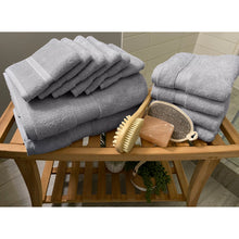 Load image into Gallery viewer, Twelve light gray spa collection towels folded on a table beside of a shower. 

